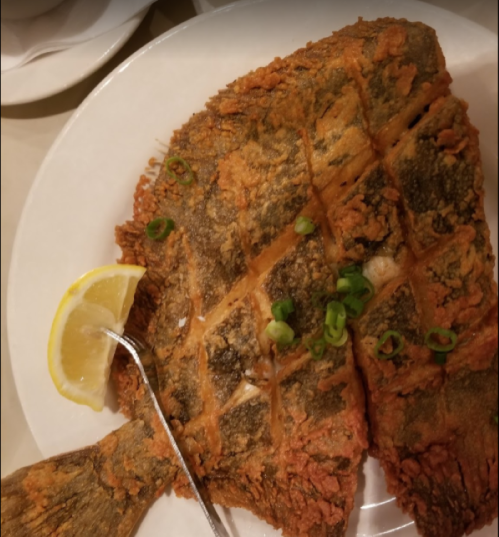 A plate of crispy fried fish garnished with green onions and a lemon wedge.