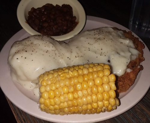 A plate of fried chicken with gravy, served with corn on the cob and a side of baked beans.