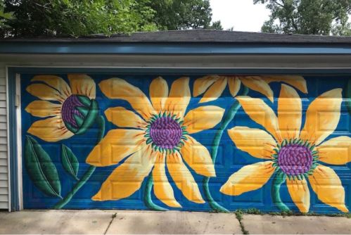 Colorful mural of large sunflowers on a garage door, featuring vibrant yellow petals and purple centers against a blue background.