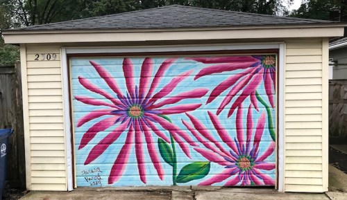 Colorful mural of large pink flowers on a garage door, set against a light blue background.