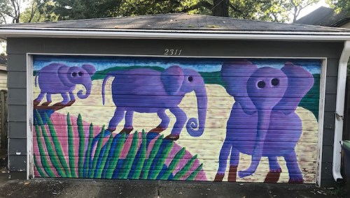 Colorful mural of purple elephants on a garage door, surrounded by green grass and a bright background.