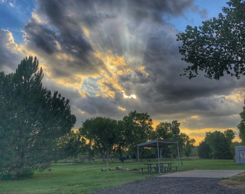 A serene park scene with trees, a picnic shelter, and rays of sunlight breaking through clouds at sunset.