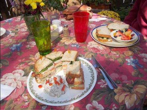 A table set with colorful drinks and two plates of sandwiches, surrounded by flowers and a floral tablecloth.