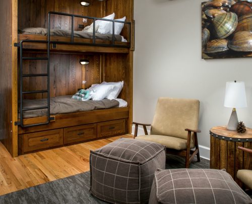 Cozy room with a wooden bunk bed, a chair, poufs, and a decorative wall art featuring seashells.