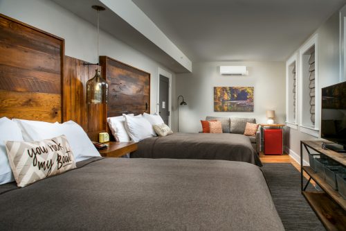 Cozy hotel room with two beds, wooden accents, a small fridge, and a seating area, featuring warm lighting and decor.