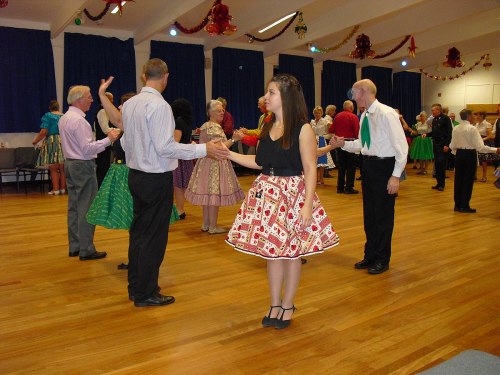 A lively dance event with people in colorful outfits, dancing and socializing in a decorated hall.