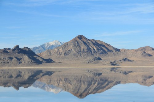 A serene landscape featuring mountains reflected in calm water under a clear blue sky.