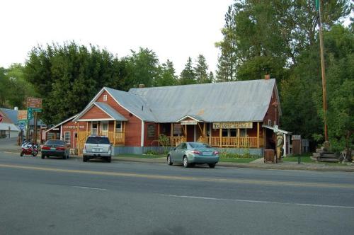A red building with a metal roof, featuring a porch, surrounded by trees and parked cars along a quiet road.