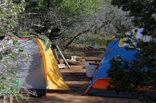 Two tents in a wooded campsite, with a grill and picnic table visible in the background.
