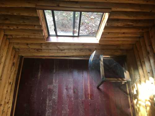 Interior of a rustic wooden cabin with a glass table and a window letting in natural light.
