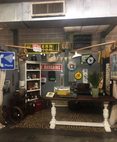 A vintage-themed shop display featuring rustic decor, signs, and a wooden table on a zebra print rug.