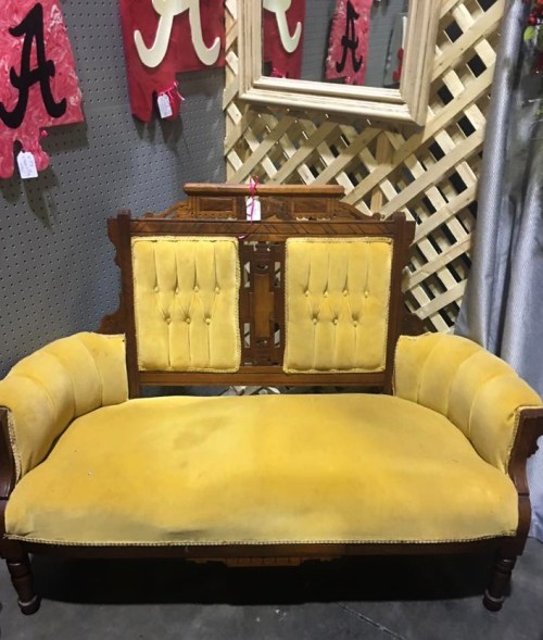 A vintage yellow upholstered settee with wooden accents, displayed against a textured background with decorative elements.