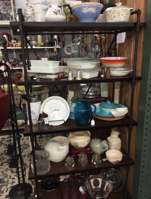 A wooden shelf displaying various vintage kitchenware, including bowls, glassware, and decorative items.