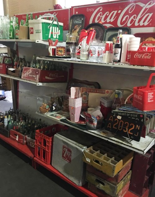A vintage display shelf filled with Coca-Cola memorabilia, glass bottles, and retro items in a nostalgic setting.