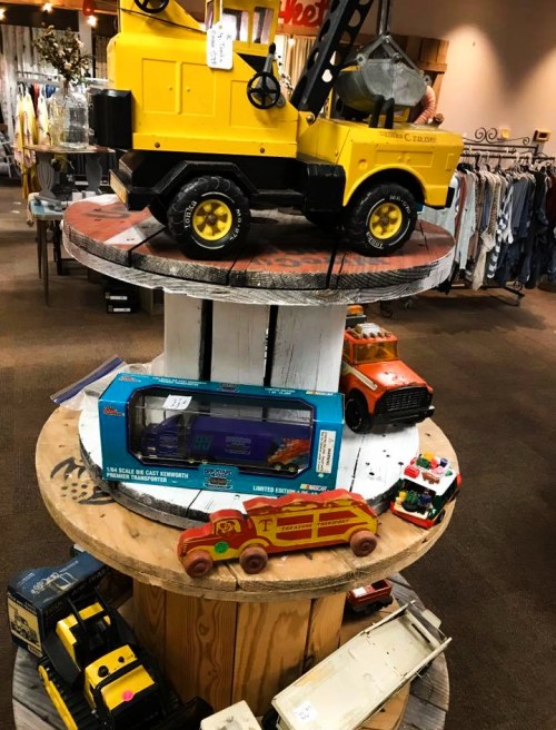 A display of vintage toy vehicles, including trucks and cars, arranged on a wooden circular stand in a store.