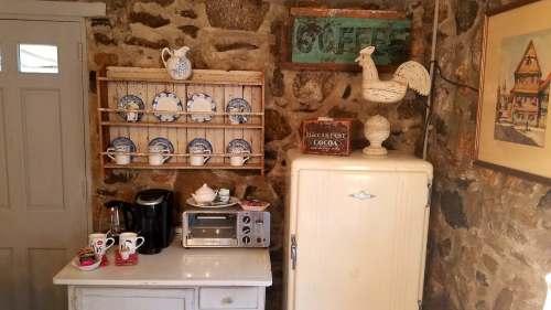 Cozy kitchen corner with stone walls, vintage fridge, coffee maker, and decorative plates on a wooden shelf.