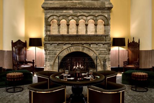 Cozy lounge with a stone fireplace, elegant seating, and a round table set for a card game. Warm, inviting atmosphere.