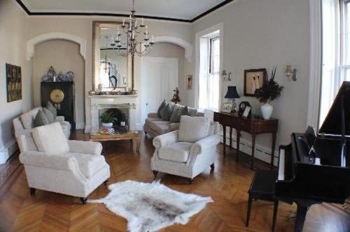 Cozy living room with light-colored furniture, a grand piano, and a decorative mirror, featuring wooden flooring and soft accents.