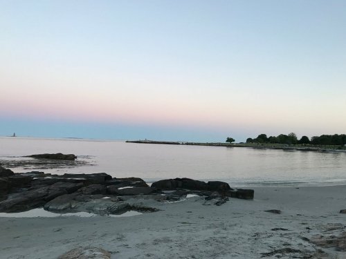 Serene beach scene at dusk, featuring calm waters, rocky shore, and a pastel sky.