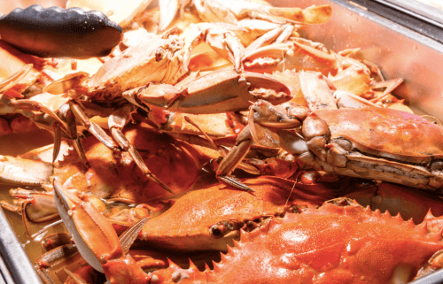 A close-up of cooked crabs piled together in a metal tray, showcasing their orange shells and claws.