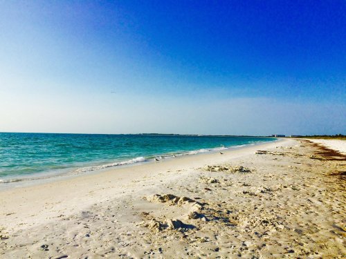 A serene beach scene with soft white sand, gentle waves, and a clear blue sky.