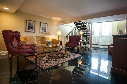 Cozy living area with a sofa, two chairs, a coffee table, and a staircase, featuring elegant decor and polished floors.