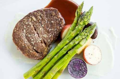 A plated dish featuring a slice of beef, asparagus, and colorful radishes drizzled with sauce.
