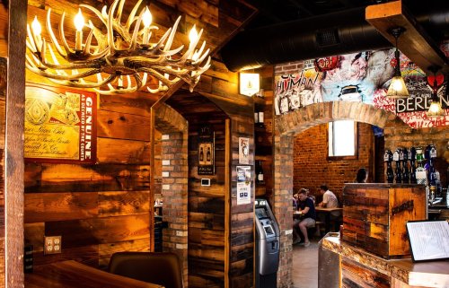 Cozy interior of a rustic bar with wooden walls, a chandelier, and patrons enjoying drinks in the background.