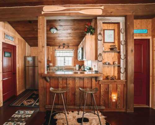 Cozy wooden kitchen with bar stools, rustic decor, and red doors, featuring a fridge and a warm, inviting atmosphere.