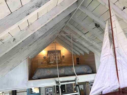 Cozy loft bedroom with a bed, wooden beams, and a sailboat decoration in a rustic interior.