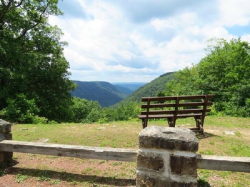 A scenic view from a lookout point, featuring a bench and lush green hills under a partly cloudy sky.