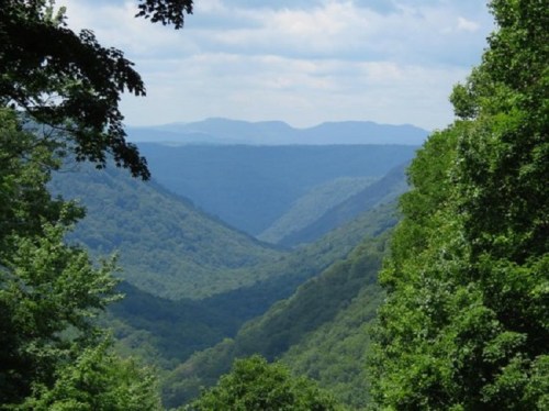 A lush green valley surrounded by mountains under a partly cloudy sky.
