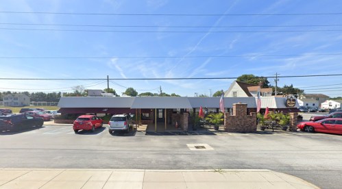 A restaurant with a brick exterior and a gray awning, surrounded by parked cars under a clear blue sky.