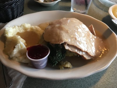 Plate of turkey with gravy, mashed potatoes, and a side of cranberry sauce, garnished with broccoli.