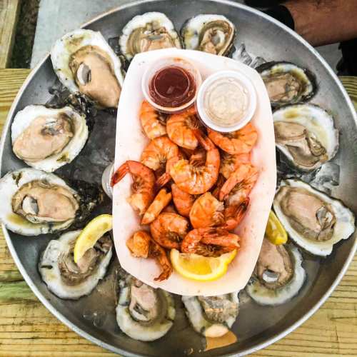 A seafood platter featuring oysters on ice and a tray of shrimp with dipping sauces and lemon wedges.