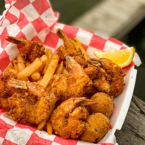 A tray of golden fried shrimp, French fries, and hushpuppies, garnished with a lemon wedge on a checkered paper.