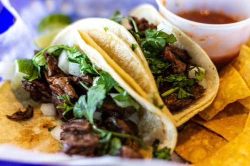 Two tacos filled with beef, onions, and cilantro, served with tortilla chips and a side of salsa.