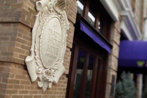 Sign of the Batty House Hotel, established in 1831, mounted on a brick wall with a purple awning in the background.