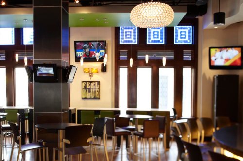 A modern bar interior with tables, colorful decor, and multiple screens displaying sports events.