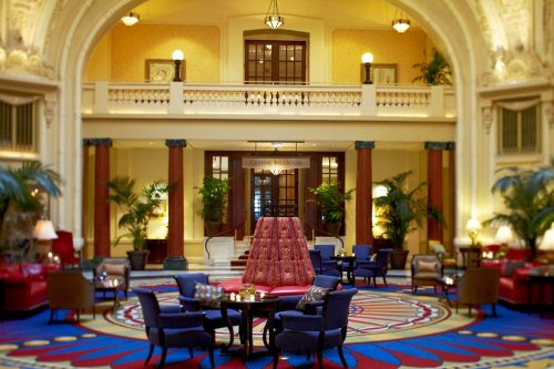 Elegant hotel lobby with plush seating, decorative plants, and a grand staircase leading to the upper level.