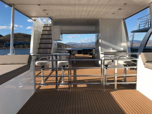 A spacious boat deck with wooden flooring, seating areas, and a view of mountains and water in the background.