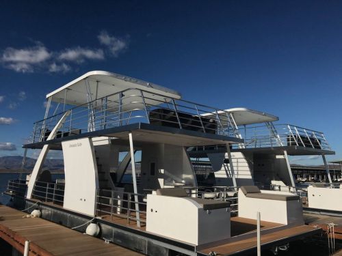 Two modern houseboats docked at a marina under a clear blue sky, featuring spacious decks and sleek designs.