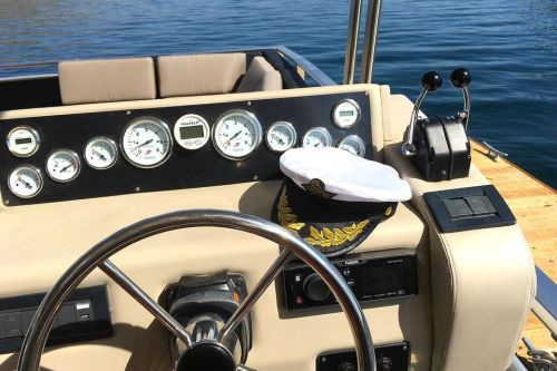 A boat's steering wheel and dashboard with gauges, featuring a captain's hat resting on the console.
