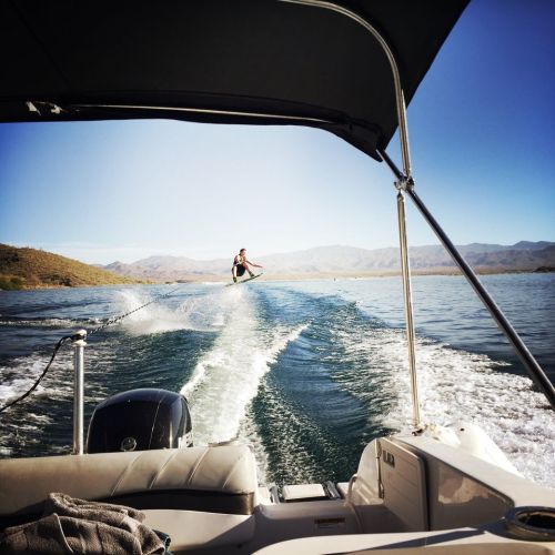 A person water skiing behind a boat on a calm lake, with mountains in the background and clear blue skies.