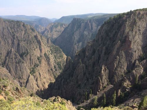A breathtaking view of a deep canyon surrounded by steep, rocky cliffs and lush greenery under a clear sky.
