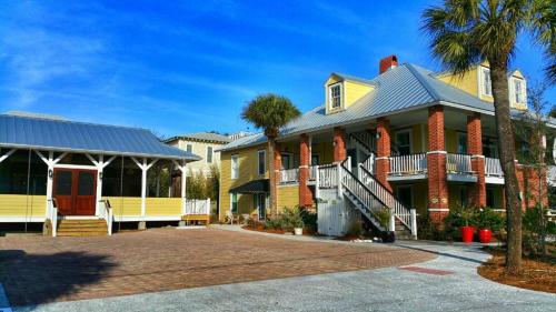 A charming yellow and brick building with a metal roof, surrounded by palm trees and a paved courtyard.