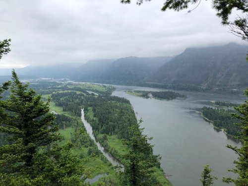 A scenic view of a winding river surrounded by lush greenery and mountains under a cloudy sky.