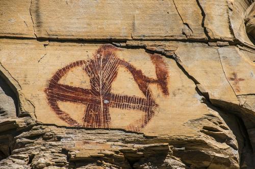 Ancient rock art featuring a circular design with intersecting lines, etched into a sandstone surface.