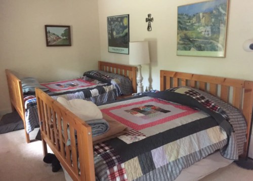 A cozy bedroom with two wooden beds, each with colorful quilts, a lamp, and framed artwork on the walls.