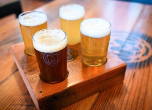 Four glasses of beer in a wooden flight tray on a wooden table.